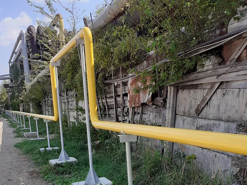 Conductă galbenă de gaze naturale de înaltă presiune pe suporți metalici, de-a lungul unui gard
